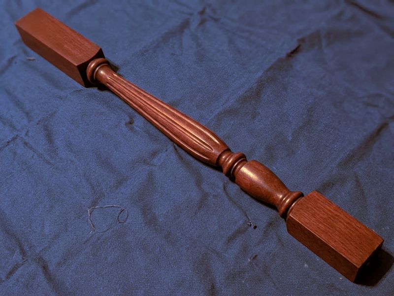 A single turned spindle on navy cloth, showing the stained finish.