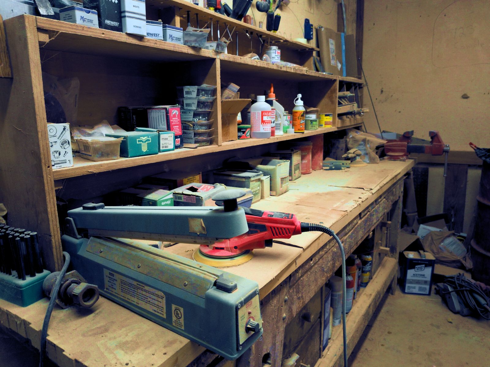 A repair bench in the shop, with a disc sander, clamps and shelves of finishing materials.